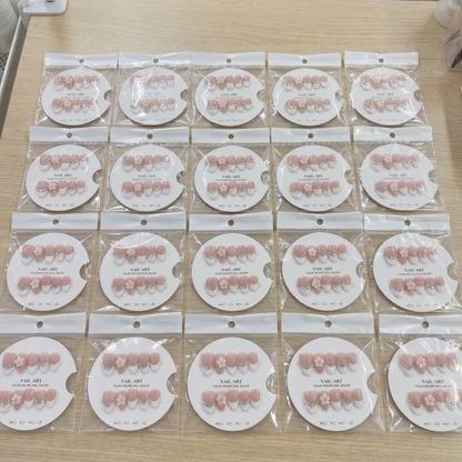 A complete set of almond-shaped white French tip press on nails with 3D daisies and rhinestones, organized by size on display cards.